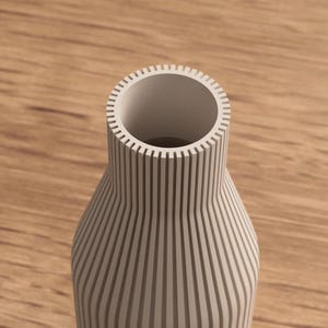 May include: A cream-colored vase with vertical, evenly spaced grooves. The vase has a wide opening and a rounded body, set against a wooden surface. The design is modern and minimalist, suitable for home decor.