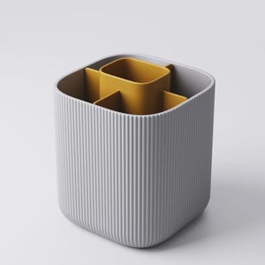 May include: A grey, ribbed desk tidy with a mustard yellow interior. The organiser has a square shape with rounded corners and vertical lines on the exterior. The interior is divided into three compartments.