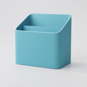 Puede incluir: Un organizador de escritorio azul claro con un exterior acanalado. El organizador tiene dos compartimentos y una parte superior inclinada. El producto est&aacute; hecho de un material s&oacute;lido y est&aacute; dise&ntilde;ado para guardar &uacute;tiles de oficina.