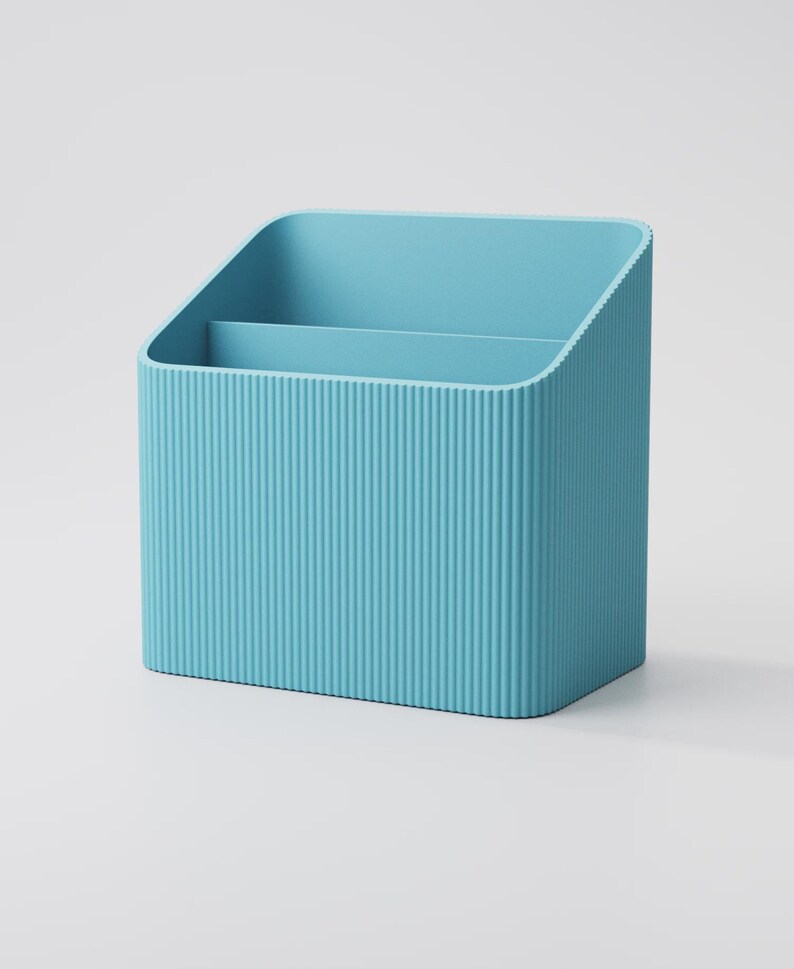 Puede incluir: Un organizador de escritorio azul claro con un exterior acanalado. El organizador tiene dos compartimentos y una parte superior inclinada. El producto est&aacute; hecho de un material s&oacute;lido y est&aacute; dise&ntilde;ado para guardar &uacute;tiles de oficina.