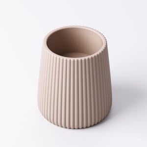May include: A beige, ribbed ceramic vase with a rounded base and a wide opening. The vase has vertical grooves running from the base to the rim. The neutral color and simple design make it suitable for various decor styles.