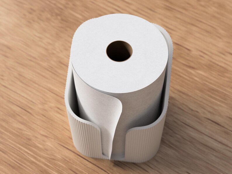 Op de afbeelding: Een witte papieren rol zit in een lichtgrijze houder met verticale ribbels. De houder staat op een houten oppervlak. De papieren rol heeft een donker centraal gat en een deel van het papier is afgerold.