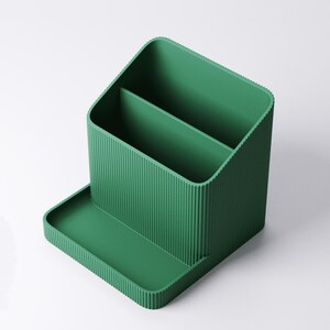 May include: A green desk organizer with a ribbed texture. The organizer has two compartments and a small tray in the front. The design is modern and minimalist, suitable for office or home use.