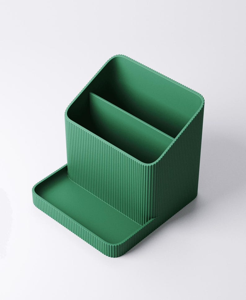 May include: A green desk organizer with a ribbed texture. The organizer has two compartments and a small tray in the front. The design is modern and minimalist, suitable for office or home use.