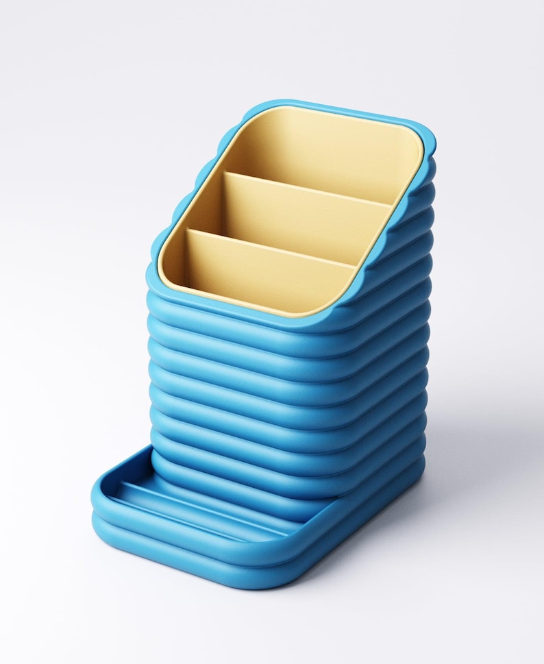 May include: A blue desk organizer with a tiered design. The organizer has three interior compartments in a yellow color and a small tray at the base. The exterior features a ribbed texture.