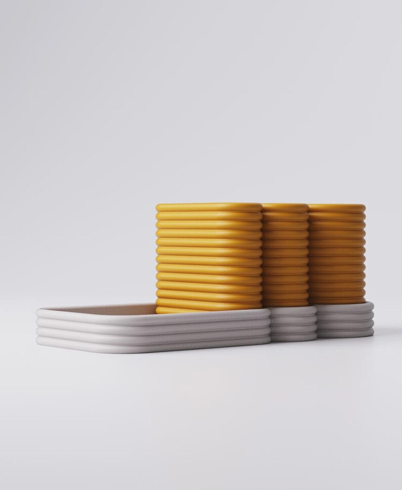 Puede incluir: Dise&ntilde;o moderno y minimalista con tres pilas de objetos rectangulares amarillos y acanalados, apoyados sobre una bandeja rectangular gris claro. Los objetos tienen un aspecto liso y redondeado, creando una est&eacute;tica limpia y contempor&aacute;nea.