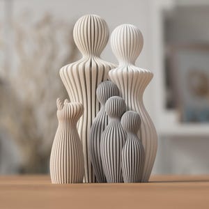 Puede incluir: Una familia de esculturas de madera en varios tama&ntilde;os y tonos de blanco y gris. Las esculturas est&aacute;n talladas con l&iacute;neas verticales, creando un efecto rayado. Las esculturas m&aacute;s altas se asemejan a figuras humanas.
