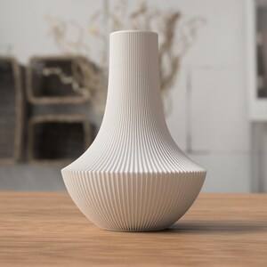 May include: A white, ribbed ceramic vase with a flared base and a slender neck. The vase is displayed on a wooden surface, showcasing its elegant, minimalist design. The vase's vertical ribbing adds texture and visual interest to the decorative piece.