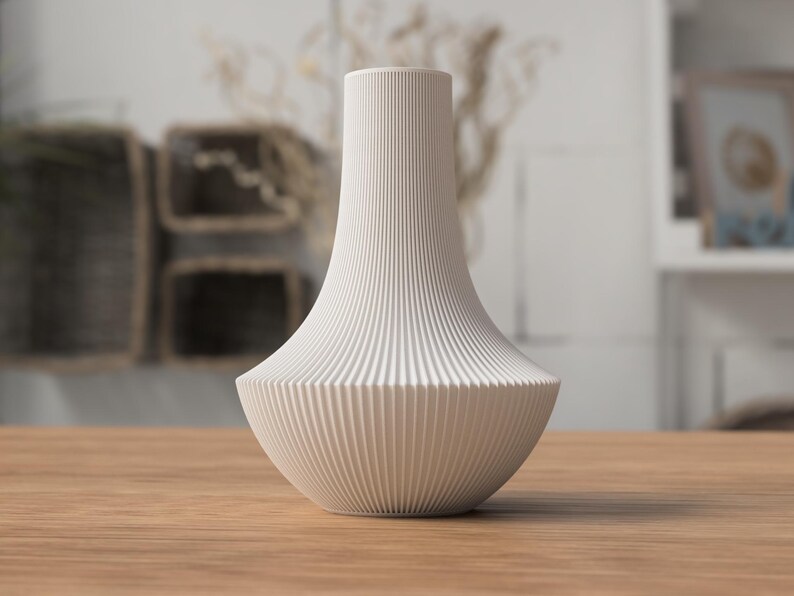 May include: A white, ribbed ceramic vase with a flared base and a slender neck. The vase is displayed on a wooden surface, showcasing its elegant, minimalist design. The vase's vertical ribbing adds texture and visual interest to the decorative piece.
