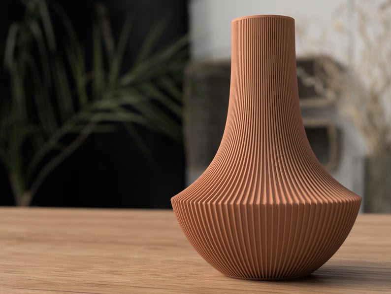 May include: A terracotta-colored vase with a ribbed, textured surface. The vase has a wide base that tapers to a narrow neck. The vase is sitting on a wooden surface.