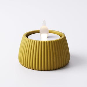 May include: A yellow, ribbed, battery-operated candle with a white interior and a flickering, flame-shaped light. The candle has a rounded, flared shape and is designed to resemble a traditional candle.