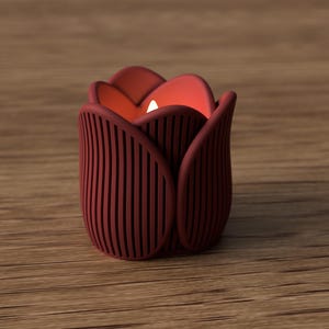 May include: A burgundy tulip-shaped candle holder with vertical lines, holding a lit white candle. The candle holder is made of a solid material and sits on a wooden surface. The interior of the tulip is a warm orange color.