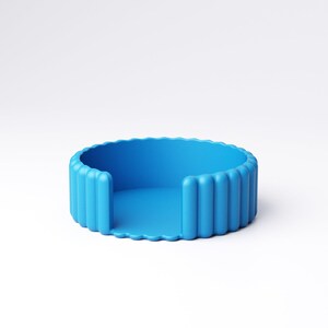 May include: A vibrant blue, circular coaster with a ridged exterior and a smooth interior. The coaster has a unique design with vertical ridges around the edge and a flat base. The object is made of a solid material and is set against a white background.