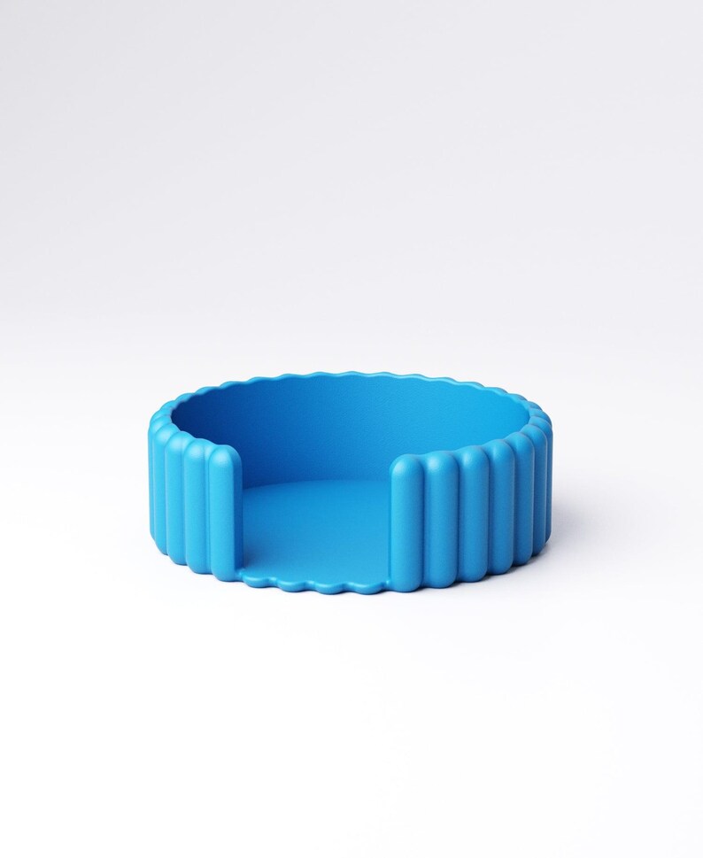 May include: A vibrant blue, circular coaster with a ridged exterior and a smooth interior. The coaster has a unique design with vertical ridges around the edge and a flat base. The object is made of a solid material and is set against a white background.