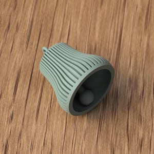 May include: A light green bell-shaped object with a rounded clapper inside. The bell has a series of vertical, curved lines on its exterior. The bell is resting on a wooden surface.
