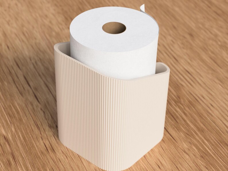 Op de afbeelding: Een beige toiletpapierhouder met een verticaal geribbeld ontwerp, met een rol wit toiletpapier. De houder heeft een gebogen bovenkant en een vierkante basis. De achtergrond is een houten oppervlak.