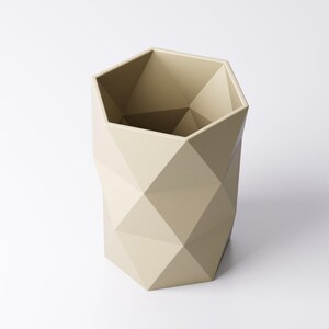 May include: A beige geometric planter with a faceted design. The planter has a hexagonal shape and is made of a solid material. The interior is a darker shade of beige. The planter is suitable for indoor or outdoor use.