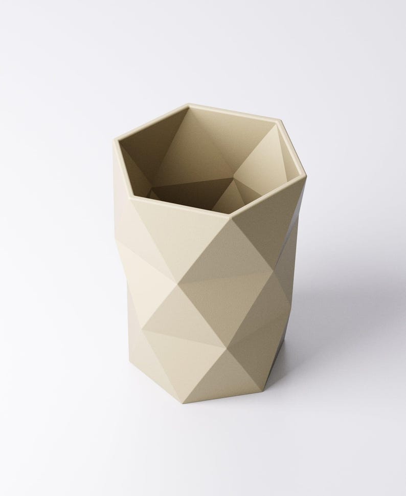 May include: A beige geometric planter with a faceted design. The planter has a hexagonal shape and is made of a solid material. The interior is a darker shade of beige. The planter is suitable for indoor or outdoor use.