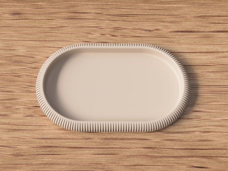 Puede incluir: Una bandeja ovalada beige con borde acanalado, sobre un fondo de madera. El dise&ntilde;o de la bandeja es sencillo y elegante, adecuado para servir o exhibir. La bandeja es de color neutro.