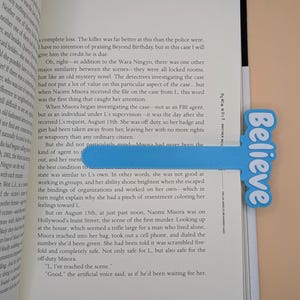 May include: A light blue bookmark with a T-shape design featuring the word Believe in white script lettering. The bookmark is placed inside an open book titled Death Note: Another Note, The Los Angeles BB Murder Cases, with visible text.