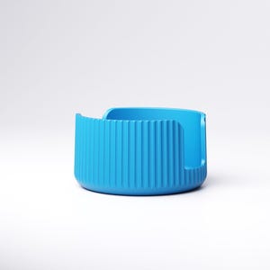 May include: A vibrant blue, modern-style container with a rounded base and vertical ridged detailing on the front. The container has a curved opening on one side and a smooth, flat back. The object is set against a plain white background.