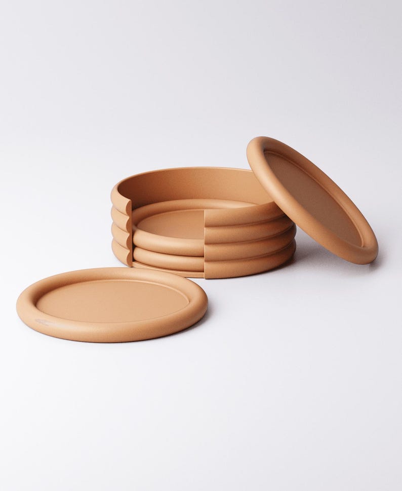 Puede incluir: Un juego de seis posavasos ovalados de color terracota con un borde elevado. Un posavasos est&aacute; separado y otro se ha retirado parcialmente de la pila. Los posavasos est&aacute;n hechos de un material liso y mate.