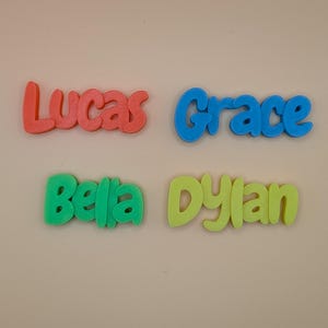 May include: Four colourful 3D-printed name signs: "Lucas" in coral, "Grace" in blue, "Bella" in green, and "Dylan" in yellow. The names are in a playful, rounded font, ideal for personalised gifts or room decor.