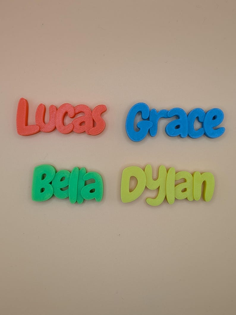 May include: Four colourful 3D-printed name signs: "Lucas" in coral, "Grace" in blue, "Bella" in green, and "Dylan" in yellow. The names are in a playful, rounded font, ideal for personalised gifts or room decor.