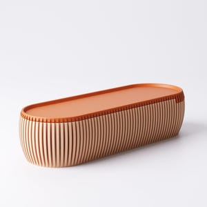 May include: A wooden, oval-shaped storage box with a flat, orange-brown lid. The sides are made of vertical, light-colored wooden slats. The box is approximately 18 inches long.