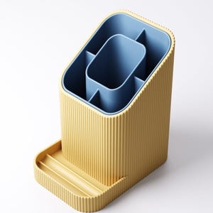 May include: A yellow and blue desk organizer with a ribbed exterior. The organizer has multiple compartments and a small tray. The interior is blue, and the exterior is yellow. The organizer is designed to hold pens, pencils, and other office supplies.