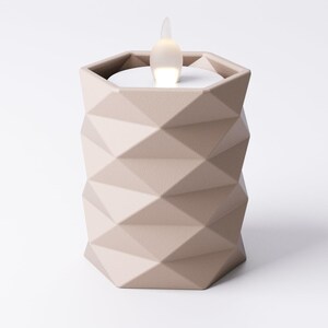 May include: A beige geometric candle holder with a flickering LED light. The candle holder has a faceted design and a hexagonal shape. The LED light resembles a flame. The candle holder is a decorative home accent.