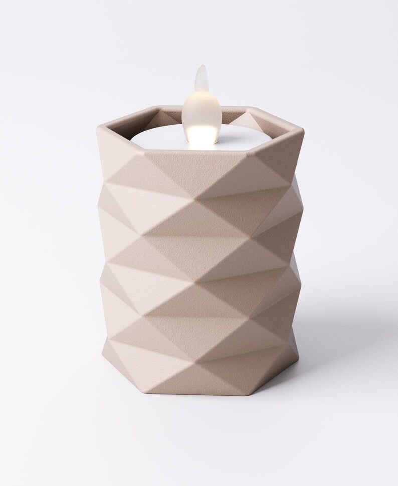 May include: A beige geometric candle holder with a flickering LED light. The candle holder has a faceted design and a hexagonal shape. The LED light resembles a flame. The candle holder is a decorative home accent.
