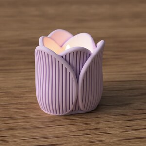 May include: A lavender tulip-shaped candle holder with vertical lines. The candle holder has a lit candle inside, emitting a warm glow. The candle holder is sitting on a wooden surface.