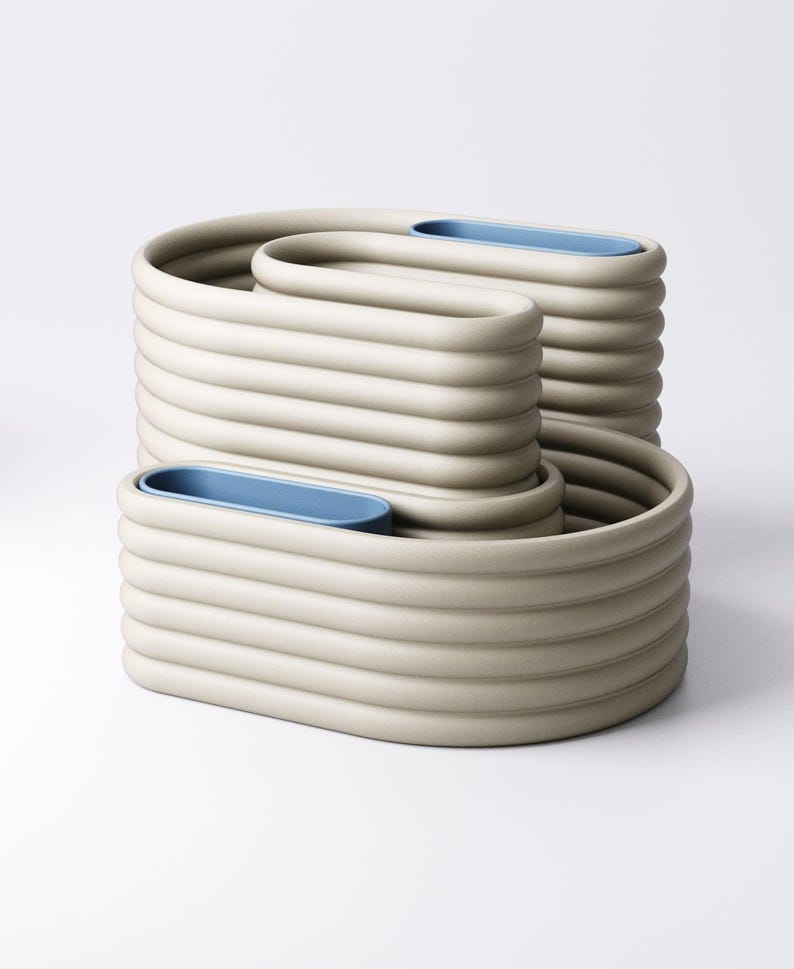 May include: Three beige ceramic containers with a unique, ribbed design. Each has a blue oval insert. The containers are stacked, creating a modern, sculptural display. The measurements are in centimetres.