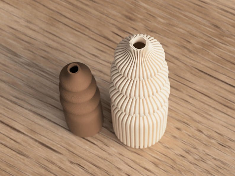 May include: Two decorative vases. One is a light beige color with a spiral design, and the other is a brown, stacked, rounded shape. Both vases have a small opening at the top. The vases are on a wooden surface.