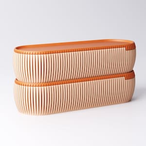 May include: Two stacked, elongated wooden containers with a light wood finish and vertical grooves. The rims and tops are a warm orange-brown color, creating a contrast. The design is minimalist and modern, suitable for storage or display.