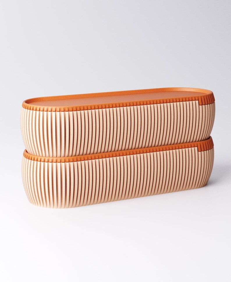 May include: Two stacked, elongated wooden containers with a light wood finish and vertical grooves. The rims and tops are a warm orange-brown color, creating a contrast. The design is minimalist and modern, suitable for storage or display.