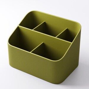 May include: Olive green desk organizer with four compartments. The organizer has a ribbed exterior and rounded corners. The compartments are divided by vertical dividers, creating separate storage spaces for office supplies or other items.