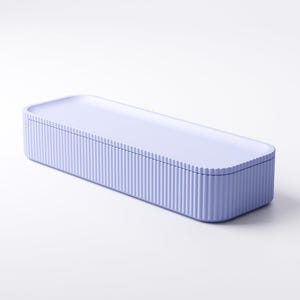 May include: A rectangular, lavender-colored storage box with a ridged exterior and a flat, matching lid. The box is designed with rounded corners and a smooth, solid top. The overall aesthetic is minimalist and modern.