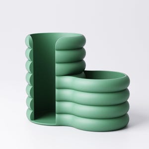 May include: A modern, green desk organizer with a unique, rounded design. The organizer features a vertical section with a curved edge and a horizontal section with a similar design. The color is a muted, pastel green.