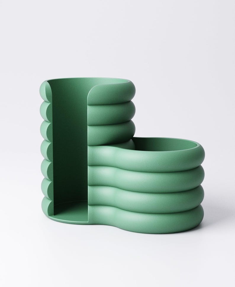 May include: A modern, green desk organizer with a unique, rounded design. The organizer features a vertical section with a curved edge and a horizontal section with a similar design. The color is a muted, pastel green.