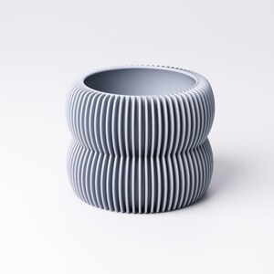 May include: A gray, ribbed ceramic planter with a unique, stacked design. The planter has a cylindrical shape with vertical grooves, creating a textured surface. The interior is smooth and the color is a muted gray.