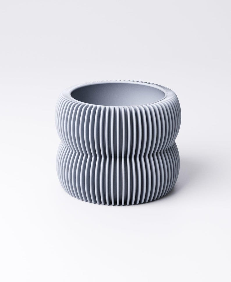 May include: A gray, ribbed ceramic planter with a unique, stacked design. The planter has a cylindrical shape with vertical grooves, creating a textured surface. The interior is smooth and the color is a muted gray.