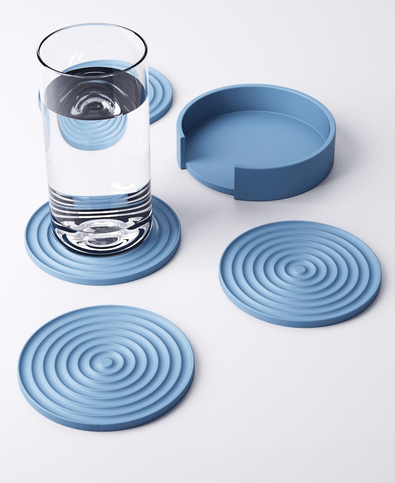 May include: A collection of four pale blue coasters with a concentric circle pattern, a matching holder, and a glass of water. The coasters are made of a solid material and are designed to protect surfaces from water rings.