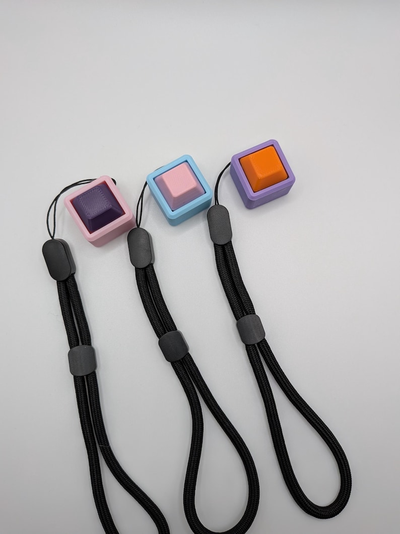May include: Three square keychains with black lanyards. Each keychain features a different color: purple with a dark purple square, light blue with a pink square, and purple with an orange square. The keychains are on a white background.