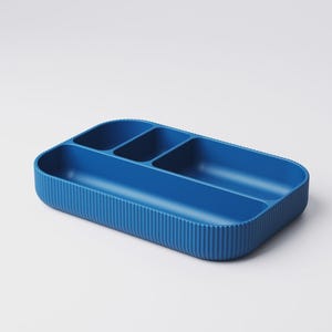 May include: A blue rectangular organizer with four compartments. The exterior features vertical ribbed detailing, while the interior has smooth, curved dividers. This storage container is designed for organizing small items.
