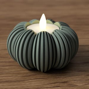 May include: A teal-colored, pumpkin-shaped candle holder with vertical grooves. The holder contains a white, glowing LED candle. The candle holder sits on a wooden surface, creating a warm, inviting ambiance.