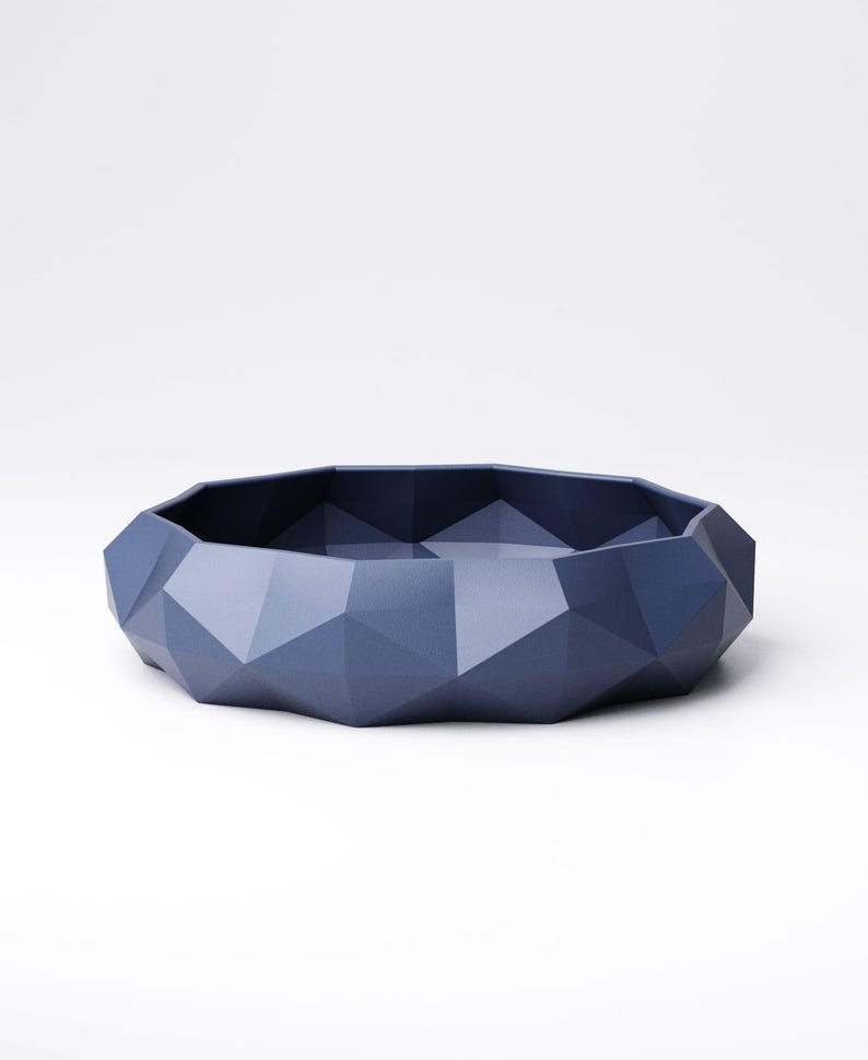 Puede incluir: Un cuenco geom&eacute;trico facetado en un tono azul apagado. El cuenco tiene un perfil bajo con una forma irregular y multifac&eacute;tica. La superficie es mate y parece estar hecho de un material s&oacute;lido. El dise&ntilde;o es moderno y minimalista.