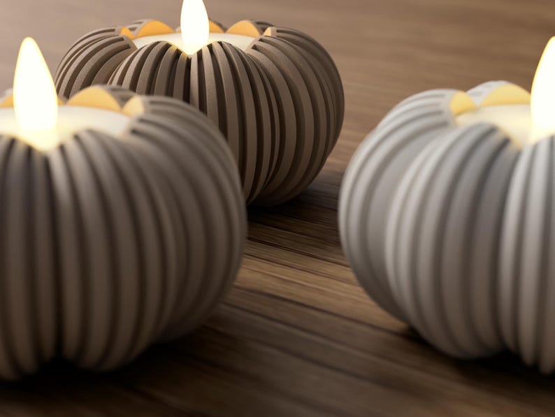 May include: Three gray, ribbed, pumpkin-shaped candle holders with lit, warm-toned LED candles. The candle holders are arranged on a wooden surface, creating a cozy and decorative ambiance. The soft glow of the candles adds a touch of warmth.