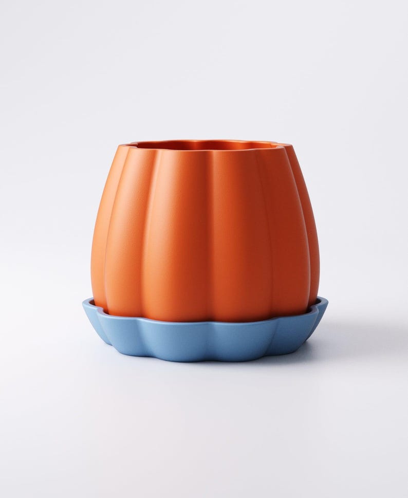 May include: Orange ceramic pumpkin-shaped planter with vertical ridges, sitting on a blue scalloped saucer. The planter has a wide opening and a smooth, glossy finish. A decorative item for home decor.